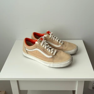 Beige Vans sneakers med orange foder - Säljer ett par beige Vans sneakers som är collab med Anaheim ducks ( pleyers only )vit sula och vit sidostripes. Insidan är orange för en cool kontrast. Skorna har snörning och platt sula, samt unikt tryck med  undersidan. 