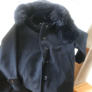 Svart skepparkavaj med päls - Säljer för inte min stil. Använd endast två gånger. Snygg svart skepparkavaj med fluffig päls runt kragen och klassisk knäppning med stora knappa från gina tricot den är för längen 146 till 152. Jackan har två fickor framtill och en stilren, rak passform som ger en cool vibe. Perfekt för dig som vill ha en varm och trendig jacka med lite extra attityd. 