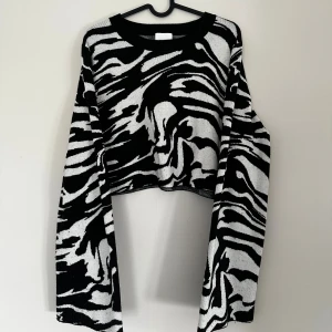 Zebramönstrad croppad stickad tröja - Säljer en croppad stickad tröja med svartvitt zebramönster. Tröjan har varit använd och därför blivit lite nopprig och lite missfärgad annars super fin!!
