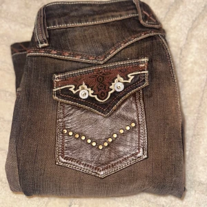 Bruna Antik Denim jeans - ❣️Priset kan diskuteras❣️ Snygga bruna bootcut vintage jeans i märket Antik Denim. Dem är väldigt unika o svåra att få tag i. Dem har bootcut passform och unika bakfickor i skinnlook, dekorerade med nitar och broderier i guld och vitt. Jeansen har kontrastsömmar och coola detaljer längs fickor och benslut. Perfekta för dig som vill sticka ut med din stil. Köpte dem för högt pris second hand och har aldrig använt dem, förra ägaren har bara använt dem några fåtal gånger så de är så gott som nya💕💕🫶🏼