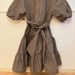 Brun rutig klänning med puffärm - Superfin brun rutig klänning med volanger och puffiga ärmar. Klänningen har knytband i midjan och en luftig, avslappnad passform. Perfekt för dig som gillar en trendig och bekväm stil med extra volym i kjolen.❤️❤️👌🤩