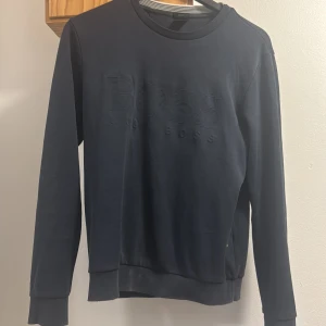 Mörkblå BOSS sweatshirt med broderad logga - Snygg mörkblå sweatshirt från BOSS med broderad logga framtill. Tröjan har rund hals, ribbade muddar och är tillverkad i mjuk bomull. Perfekt för en chill och stilren look.