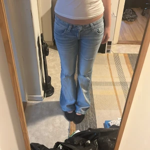 Ljusblå bootcut jeans med spetsdetaljer - Priset går att diskutera :))Säljer ett par ljusblå bootcut jeans med slitningar på benen och snygga bakfickor med spets och paljetter. Låg midja och klassisk femficksmodell. Perfekta för dig som gillar en avslappnad och trendig look.