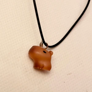 Choker Kapybara halsband Kapibara - Så gulligt halsband med en liten berlock som ser ut som en kapybara! Trädd på en svart kortare tråd, justerbar 35-40 cm. Kapybaran är ca 1,4 lång och 1 cm hög.