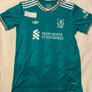 Liverpool 25/26 fotbollströja  M - Säljer en Liverpool FC fotbollströja. Tredje tröjan för säsongen 25/26. Tröjan har aldrig burits.