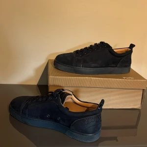 Christian Louboutin sneakers  - Snygga svarta sneakers från Christian Louboutin i mjuk mocka med klassisk röd sula och diskret logga på hälen. Skorna har rund tå, svarta snören och en stilren design som passar till det mesta. Insidan är fodrad i beige läder för extra komfort. Pris kan diskuteras, kvitto finns