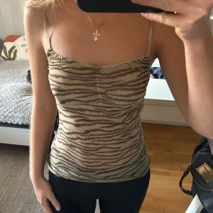 Beige zebramönstrad linnetopp - Säljer en beige linnetopp med zebramönster och tunna axelband. Toppen har en liten rosett framtill och är figurnära i modellen.  Aldrig använd 💖