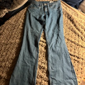 Blå flared jeans från H&M, low waist - Snygga ljusblå jeans från H&M med flared ben och låg midja. Jeansen har justerbar midja och klassisk femficksdesign. En bekväm passform. Köpta på barnavdelningen och är storlek EUR 164 