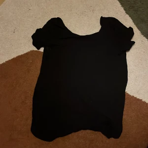 Svart topp från Gina Tricot - En enkel svart topp från Gina Tricot i storlek M. Modellen har korta ärmar och rund halsringning, perfekt för att matcha med jeans eller kjol. Materialet känns mjukt och lätt mot huden, och den har en klassisk, stilren look.