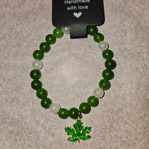 Grönt pärlarmband med lönnlöv berlock - Unikt armband med gröna och vita pärlor, dekorerat med en grön lönnlöv berlock. Stretchig design som passar de flesta handleder. Perfekt för dig som gillar naturinspirerade detaljer och vill sticka ut med ett coolt smycke. Ca 17cm 