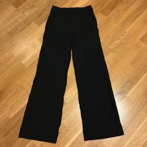 Svarta vida kostymbyxor - Svarta kostymbyxor med hög midja och riktigt breda ben. Snygg och stilren modell som passar perfekt till en trendig look. Byxorna har diskreta fickor i sidorna och är gjorda i ett mjukt tyg som faller snyggt.