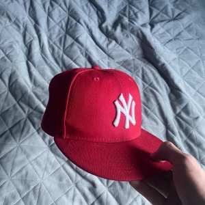 Röd New Era NY keps 59FIFTY - Snygg röd New Era 59FIFTY keps med klassiskt New York Yankees broderat i vitt framtill. Platt skärm och broderad MLB-logga baktill. Tillverkad i 100% polyester, perfekt för dig som vill ha streetstyle med sportig vibe.