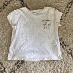 Vit t-shirt med stjärna och text - Vit t-shirt i bomull med svart tryck av stjärna och texten 'MA CHÉRIE' både fram och bak. Klassisk rund hals och korta ärmar. Enkel och chill stil som passar perfekt till jeans eller shorts.