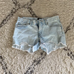 Ljusblå jeansshorts med slitningar - Säljer ett par ljusblå jeansshorts från 157 med råa, fransiga kanter och slitna detaljer framtill. Klassisk femficksmodell med knapp och dragkedja. Perfekt för dig som gillar en chill och avslappnad stil.