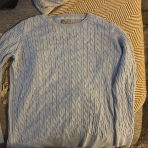 Ljusblå kabelstickad tröja Basic You - Kabelstickad ljusblå tröja från Basic You i ekologisk bomull. Tröjan har rund halsringning, ribbade muddar och lång ärm. Perfekt för dig som gillar en klassisk och stilren look med en soft vibe.