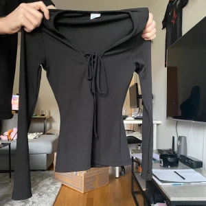Svart ribbad långärmad topp med snörning - Säljer en svart långärmad topp med ribbad struktur och snygg snörning framtill vid halsen. Toppen har en smickrande passform och är perfekt att styla med jeans eller kjol. Materialet är mjukt och stretchigt för extra komfort.