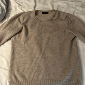 Beige merinoulltröja från J.Lindeberg - Snygg beige stickad tröja från J.Lindeberg i 100% merinoull. Tröjan har rund hals, diskret broderad logga på bröstet och ribbade muddar vid ärmslut och nederkant. Perfekt för dig som gillar stilrena och mjuka plagg. Storlek S borde nog passa också 