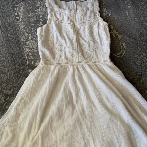 Vit ärmlös sommarklänning med spets - Superfin vit klänning med broderad spets upptill och luftig, lätt kjol. Ärmlös modell med rund halsringning och vackra detaljer. Perfekt för varma dagar och ger en romantisk vibe.
