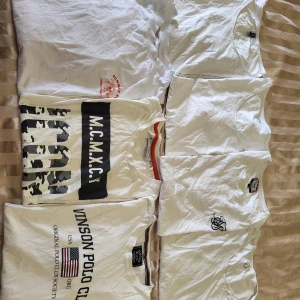 Parti 7-pack vita t-shirts med tryck - PARTI vita t-shirts i olika stilar, vissa med tryck som 'Vinson Polo Club' och amerikansk flagga, 'M.C.M.X.C.V' med camo-detaljer, samt en med rött 'Summer Sun' tryck. Märken inkluderar Vinson Polo Club, H&M och 19FIVE. Alla har rund hals och klassisk passform.