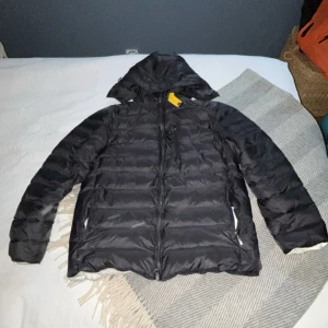Svart puffer/dunjacka från Parajumper - Säljer en svart dunjacka från Parajumpers, storlek Large. Jackan har huva, dragkedja framtill och fickor med dragkedja. Insidan är ljus och har coola detaljer med etiketter och text. Perfekt för kalla dagar. Dragkedjan på en av fickorna är trasiga. Kan gå ned i pris vid snabb affär!