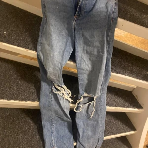 Blå ripped jeans från Zara - Säljer ett par blå jeans från Zara med snygga slitningar och stora hål vid knäna. Bootcut