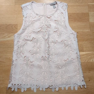 Ljusrosa/Beige spetsblus från H&M XS - Supersöt ljusrosa/beige blus från H&M i storlek XS. Blusen är ärmlös och har ett detaljerat broderat spetsmönster med blommiga inslag och en fin kant nedtill. Stängs med dragkedja i ryggen. Perfekt för dig som gillar romantiska vibes.