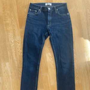 Mörkblå jeans från Acne - Mörkblå jeans från Acne med klassisk femficksdesign, smal passform och snygga kontrastsömmar. Byxorna har normal midja och raka bakfickor, smala ben, tillverkade i något stretchig bomullsdenim. Storlek 27/34. Perfekta för dig som gillar stilrena och tidlösa jeans.