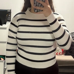 Randig ribbstickad tröja i svart och vitt - Tröjan har lång ärm, rund halsringning och sitter snyggt figurnära. Perfekt för dig som gillar klassisk stil med en modern twist.