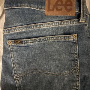 Lee Daren Zip Fly jeans blå W32 L34 - Säljer ett par klassiska Lee Daren Zip Fly jeans i blå tvätt. Modellen har rak passform med normal midja och dragkedja. Jeansen har snygga detaljer som Lee-märke på bakfickan och brunt läderpatch i midjan. Perfekt för dig som gillar en tidlös jeansstil.