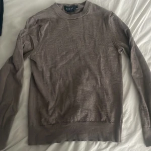 Brun merinoulltröja från Riley - Säljer en stilren brun långärmad tröja från Riley i mjuk merinoull. Tröjan har rund hals och en clean look utan mönster eller detaljer, perfekt för dig som gillar enkel och klassisk stil. Passar dig som vill ha något bekvämt och snyggt. Är öppen för frågor, priset går att diskutera. Säljer för att den krympte.