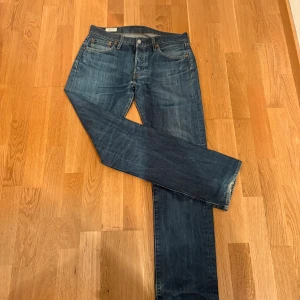Levi's 501  - Klassiska Levi's 501 jeans i blå denim med raka ben och femficksmodell. Snyggt slitna detaljer och ikonisk läderpatch bak i midjan. Jeansen har normal passform och är tillverkade i bomull. Perfekta för en avslappnad och tidlös look. 