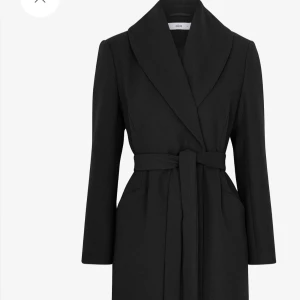 Svart kappa med bälte från Ellos - Stilren svart kappa från Ellos med bred krage och knytskärp i midjan. Långärmad modell diskreta fickor i sidorna. Perfekt för dig som gillar en klassisk look med modern twist. Gjord av filtad ullmix   - Stängning med dold tryckknapp   - Två fickor   - Avtagbart knytskärp i midjan   - Vävt, slätt foder   - Slits bak   - Längd: 120 cm i storlek 36 Kappan är inte för lång, den går strax nedanför anklarna och följer kroppens linje. Den har ett midjebälte som ger form.