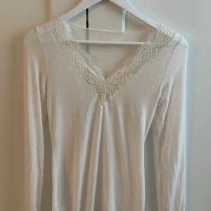 INTIMISSIMI Vit långärmad topp med spets - Säljer en vit långärmad topp med v-ringning och fina spetsdetaljer runt halsen. Toppen är i mjukt material och har en feminin och enkel design som passar perfekt till jeans eller kjol. Ordinarie pris 559kr