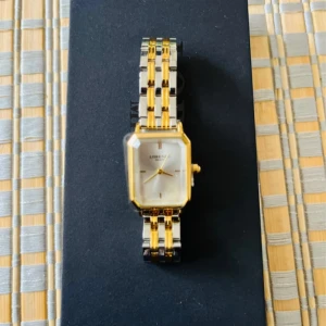 Elegant damklocka  - Stilren och elegant klocka från Lorenzo med rektangulärt ur och länkarmband i guld och silver. Urtavlan är vit/silver med minimalistiska detaljer och guldfärgade visare. Armbandet har en cool tvåfärgad design och klockan levereras med extra länkar, verktyg och certifikat.  Ord. Pris: 1695kr