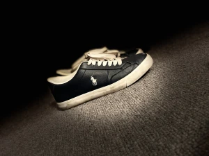 Mörkblå sneakers från Polo Ralph Lauren - Snygga mörkblåa sneakers från Polo Ralph Lauren med vit logga på sidan och vita detaljer. Skorna har rund tå, vita snören och vit sula. Tillverkade i skinnliknande material och kommer med extra mörkblå skosnören. Perfekta för en clean och klassisk stil.