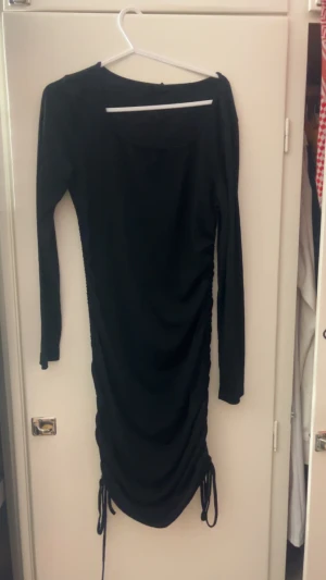 Svart långärmad klänning från Shein - Svart långärmad klänning från Shein i storlek M. Klänningen har en tight passform och snygga snörningsdetaljer längs sidorna som ger en cool look. Materialet är mjukt och stretchigt, perfekt för dig som gillar stilrena och enkla plagg.