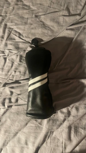 Svart golf headcover - Säljer ett svart golf headcover med två vita diagonala ränder på framsidan. Perfekt för dig som vill skydda din golfklubba från onödiga skador. 