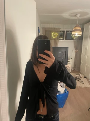 Svart omlottopp med knyt från Gina Tricot - Säljer en svart omlottopp från Gina Tricot i storlek XS. Toppen har lång ärm, djup v-ringning och en snygg knytning framtill som ger en croppad look. Perfekt att styla med jeans eller kjol för en trendig outfit.
