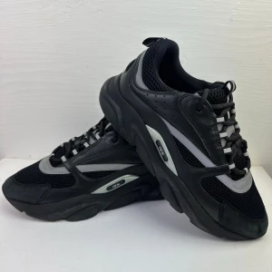 Svarta sneakers med grå detaljer - Säljer ett par Dior b22 Tripple black som slutat säljas. Skorna är i mycket bra skick och är väldigt sällsynta. Skorna är i storlek UK 10.5 vilket motsvarar EU 44.5. 