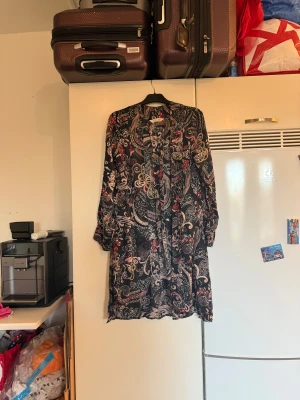 Blommig omlottväst från Odd Molly - Säljer en svart cardigan från Odd Molly med blommigt mönster i rött, beige och grått. Västen har långa ärmar och ett flowigt, avslappnat fall. Materialet är mjukt och tunt, perfekt för lager-på-lager. Snygg detalj med knyt framtill. Storlek 1 som enligt deras storleksguide motsvarar en S.  Mycket fint skick, jag hittar inga synliga anmärkningar eller defekter.  