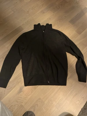 Helzip från These Glory Days - Säljer en svart kofta med hel dragkedja och hög krage. Tröjan har långärmade ärmar och är tillverkad i ett mjukt stickat material som passar perfekt för kyliga dagar. Enkel och stilren design som funkar till många olika outfits. Tröjan är från these glory days