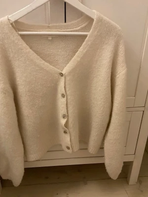 Beige stickad kofta med v-ringning.  - Vit stickad kofta med v ringning. Lite nopprig men kan noppras av innan den skickas. Önskar att jag kunde använda denna men jag blir alldeles för varm. Använd 3-4 gånger💕pris kan diskuteras.