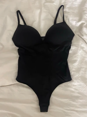 Svart body från H&M - Svart korsettbody från H&M i storlek M med justerbara axelband och vadderade kupor. Materialet är en blandning av polyamid och bomull som ger en mjuk och stretchig känsla. Snygg, figurnära passform och stilren look. Aldrig använd inte ens provad
