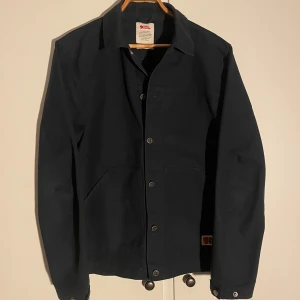 Marinblå overshirt från Fjällräven - Skick: 10/10 (använd 1 gång), Nypris: 2500kr, Storlek: L, (väldigt enkel och snygg jacka men också väldigt tålig och slitsam! Marinblå tålig overshirt från Fjällräven, modell Vardag Jacket. Klassisk design med krage, knappar framtill och två stora fickor. Tillverkad i slitstark bomull och polyesterblandning, perfekt för lager-på-lager. Snygg och enkel att matcha med jeans eller chinos.