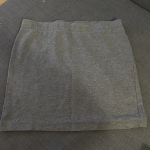 Mörkgrå kortkjol från FB Sister - Säljer en enkel och stilren mörkgrå kortkjol från FB Sister i storlek S. Kjolen har rak passform och är gjord i mjukt bomullsmaterial som känns skönt mot huden. Perfekt att matcha med en snygg topp eller hoodie för en chill look.