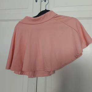 Ljusrosa bolerotopp med krage - Säljer en ljusrosa bolerotopp med korta ärmar och en snygg krage. Toppen har en flowy och lös passform som ger en cool och avslappnad vibe. Perfekt att slänga över en klänning eller linne för en extra touch.