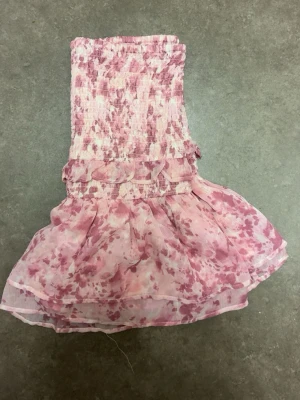 Rosa volangkjol från Gina Tricot XS - Supersöt kort kjol från Gina Tricot i storlek XS. Kjolen är ljusrosa med blommigt mönster och har smock upptill samt volangdetaljer längs midjan. Tillverkad i ett lätt och luftigt material som ger en flowy känsla. Perfekt för vår och sommar!