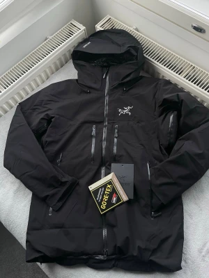 Arc’teryx Gore-Tex Waterproof Puffer Jacket – Black - Premium Arc’teryx insulated puffer jacket made with Gore-Tex technology. Fully waterproof, windproof, and breathable, designed for cold and wet conditions. Features a high-neck insulated hood, full zip closure, and multiple secure zip pockets.                           Condition:Brand new with tags Colour: Black Material: Gore-Tex (waterproof & breathable) Features: Insulated, hooded, zip pockets, premium build quality it is size s but fits for size M