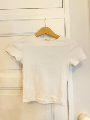 Vit t-shirt från Gina Tricot XS - En klassisk vit t-shirt från Gina Tricot, basically basics-kollektionen. Modellen är kortärmad med rund hals och har en clean, enkel look. Tillverkad i mjuk bomull som är skön mot huden. Perfekt att styla med jeans eller shorts för en chill vibe.