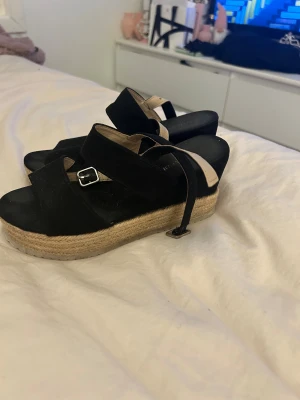 Svarta sandaler med platåsula - Snygga svarta sandaler med breda remmar och beige spänne. Skorna har en rejäl platåsula i repimitation som ger extra höjd och somrig känsla. Perfekta till jeans eller klänning när du vill ha en chill men trendig stil.